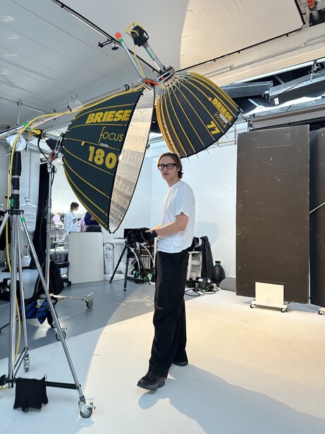 Photographer adjusting a large rectangular softbox suspended from a ceiling-mounted light stand in a studio.