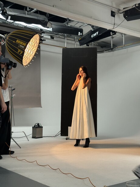 Studio fashion shoot with model in cream dress against black backdrop under large key light.