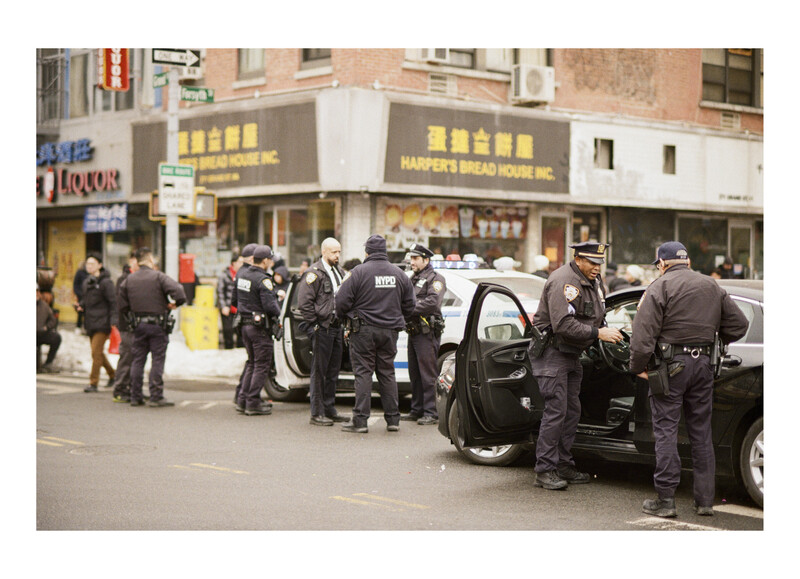 Police officers gathering around a parked vehicle on a city street lined with storefronts.