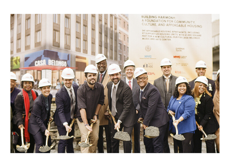 Group of officials and dignitaries in hard hats and business attire at a groundbreaking ceremony.
