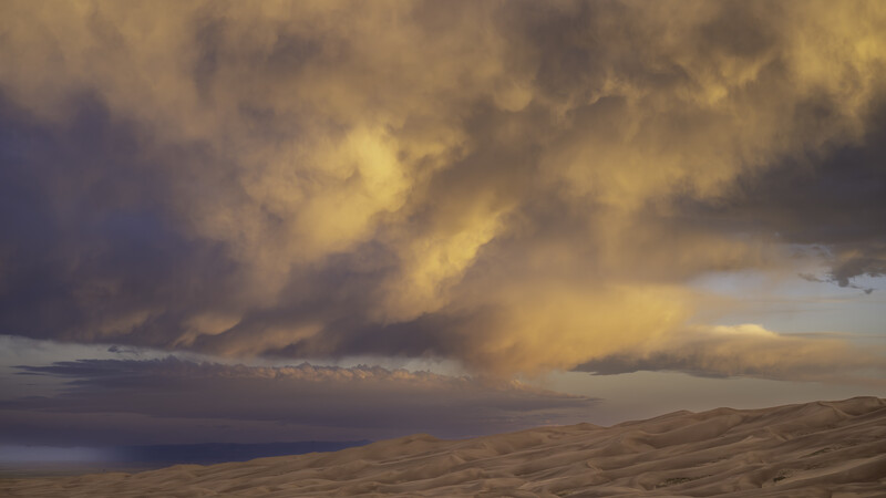 Dramatic golden storm clouds towering over a desert landscape at sunset.