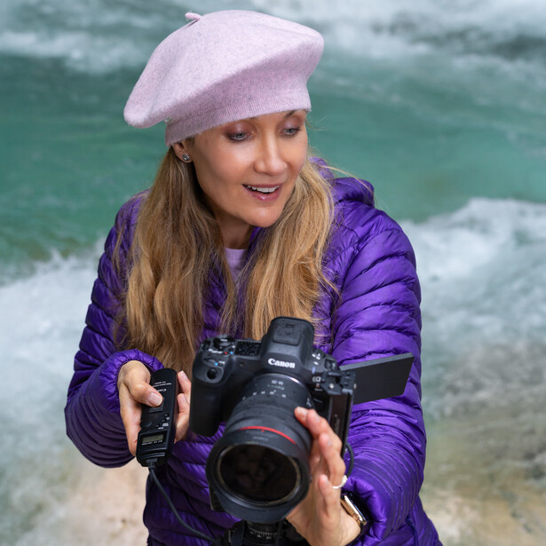 Photographer with DSLR camera at beach with turquoise water and waves behind her.
