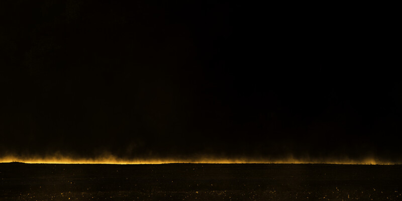 Golden light stretching across the horizon at night above a dark landscape with scattered lights below.