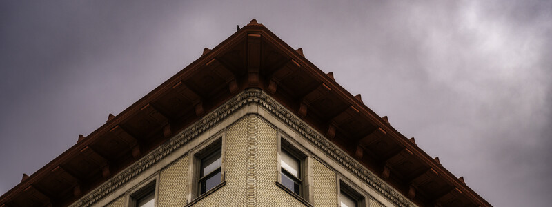 Architectural detail of a cream brick building corner with dark wooden eaves against an overcast sky.