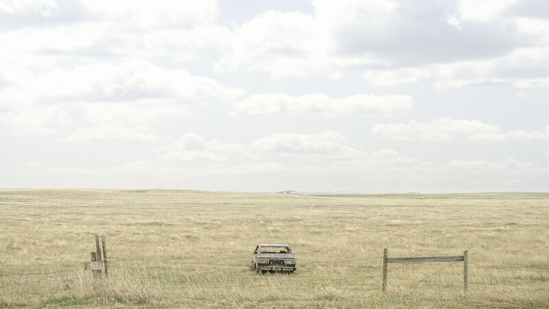 Vintage truck parked alone in a vast, flat grassland with fence posts and minimal structures visible.