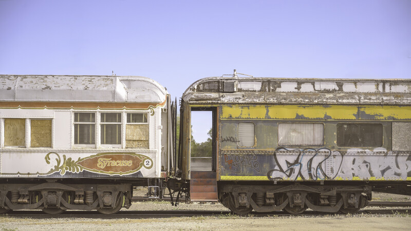 Two abandoned vintage passenger rail cars parked side by side against a clear sky.