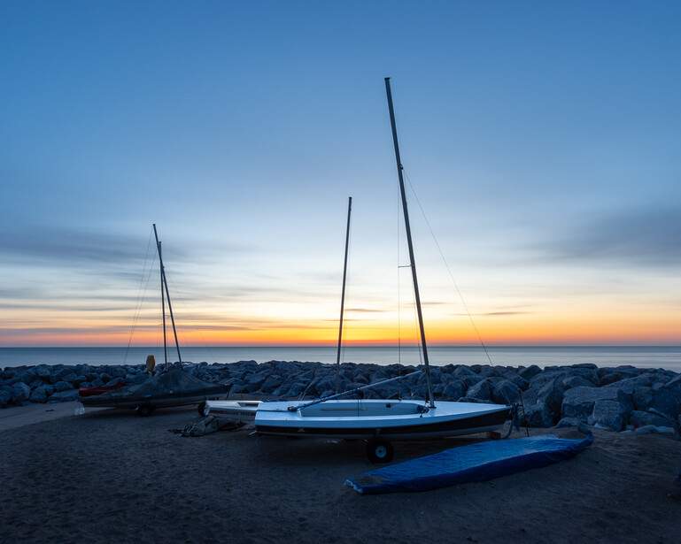 Photograph of personal sailboats on the beach at sunrise