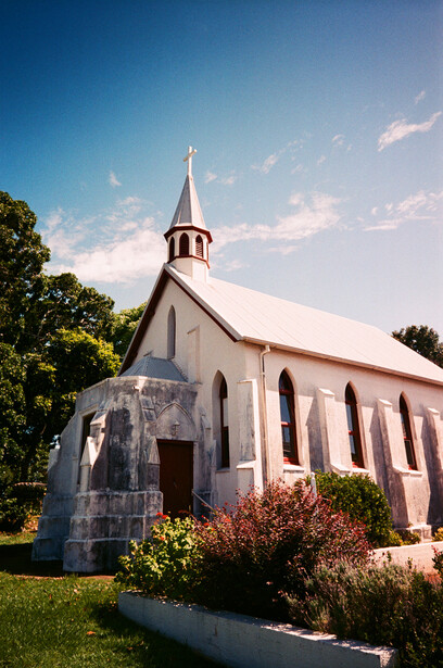 White rural church with steeple under blue sky and soft clouds, surrounded by green landscaping.