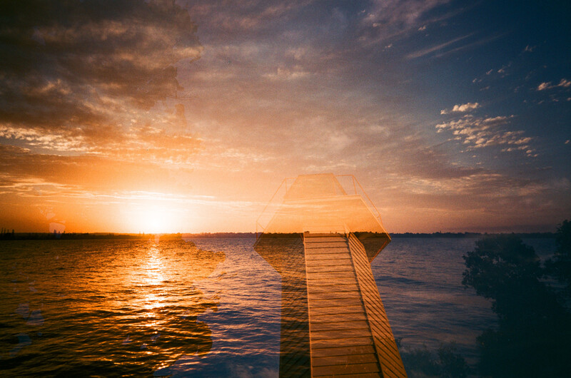 Wooden pier extending into calm water at sunset with golden sky and sun on horizon.