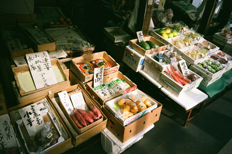 Overhead view of Japanese market produce display with wooden boxes of fresh vegetables and seafood.