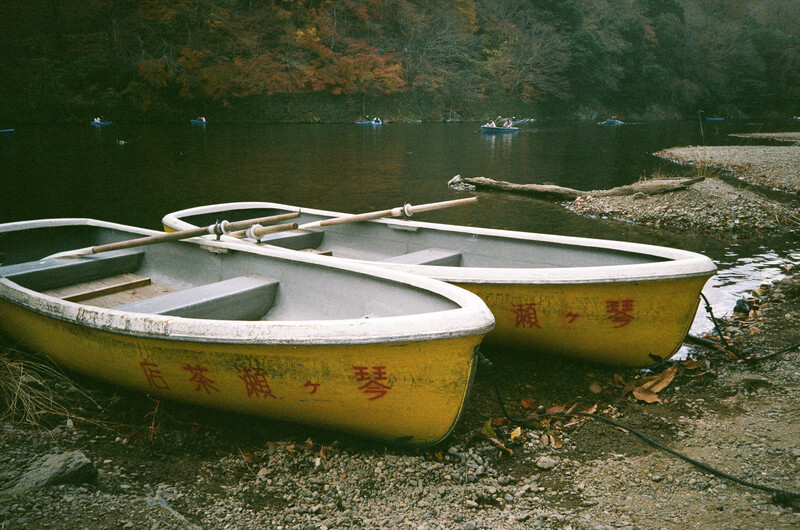 Two yellow rowboats with white trim lined up on a rocky shore next to calm water.