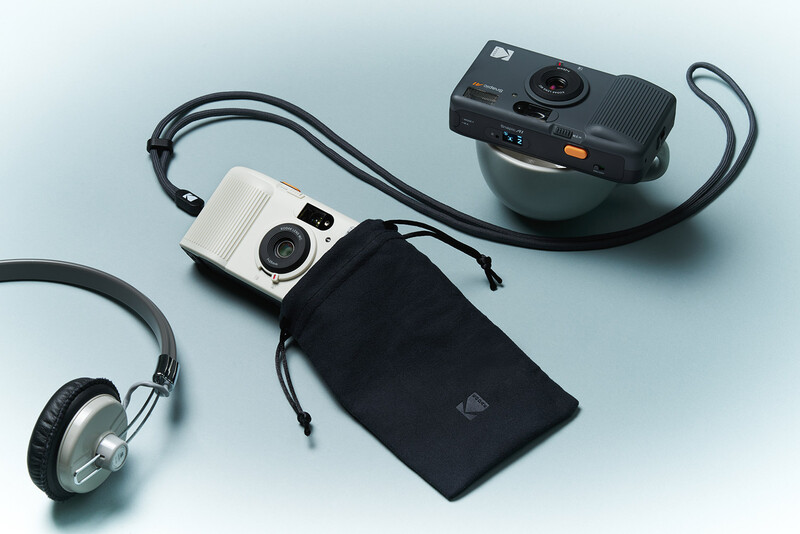 Two instant cameras with carrying case and headphones arranged on a gray surface.