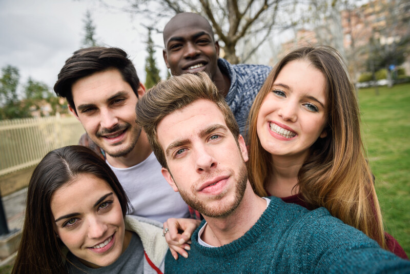 Five smiling people posing together outdoors in a park setting.