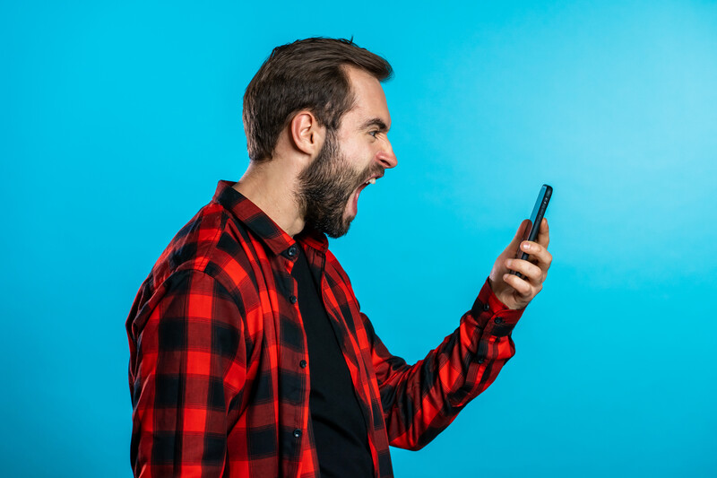 Man in red plaid shirt holding smartphone with animated expression against blue background.
