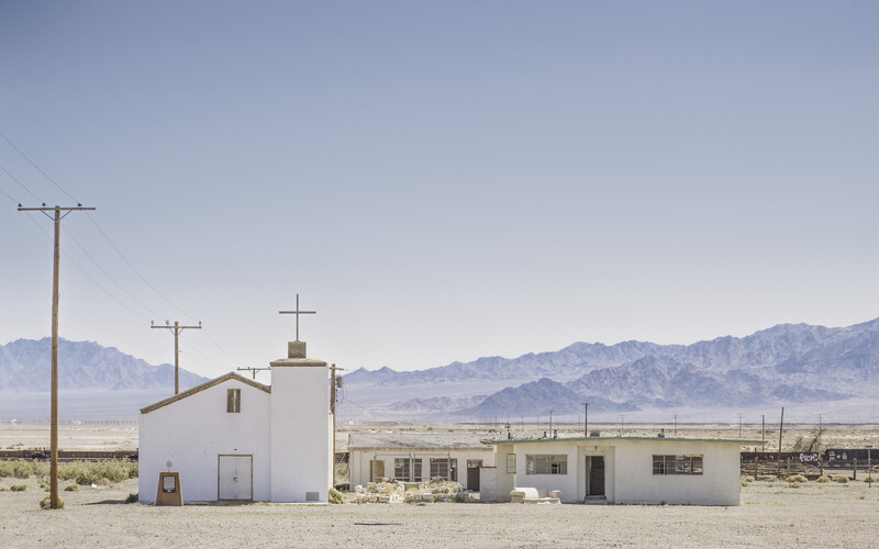 White desert structures with crosses and utility poles against distant mountains under clear sky.