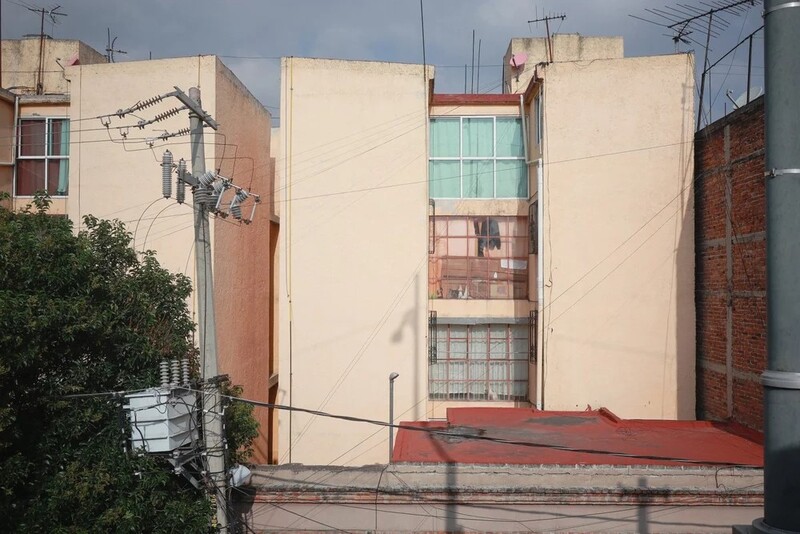 Beige apartment building with protruding brick structure and power lines against overcast sky.