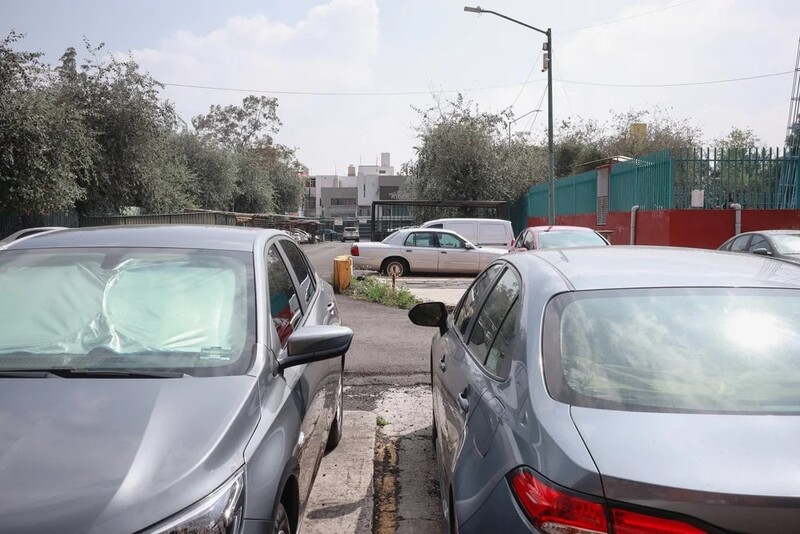 Row of parked cars in an urban lot on a sunny day with industrial buildings in the background.