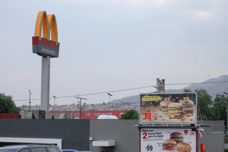 McDonald's golden arches sign mounted on tall pole above restaurant building in urban hillside setting.