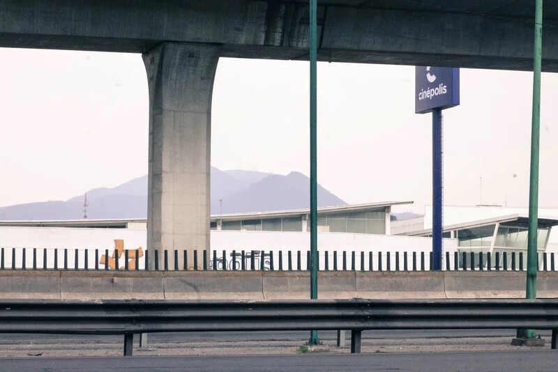 Concrete highway overpass with green metal railings and signage, mountains visible in hazy distance.