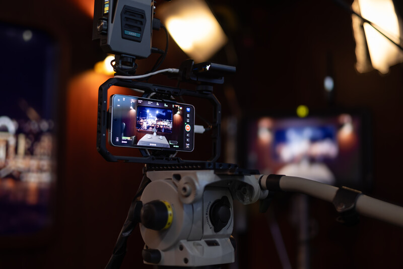 Professional cinema camera mounted on tripod with external monitor displaying live footage and mounted LED light.