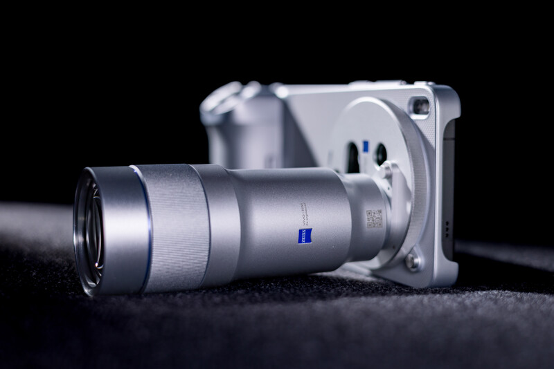 Compact mirrorless camera with attached silver telephoto lens on dark surface.