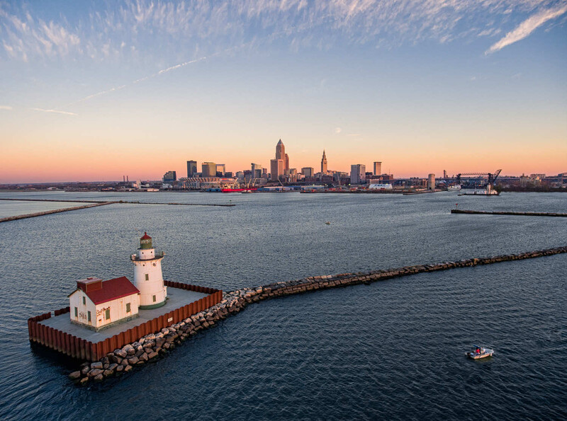 Red and white lighthouse on a breakwater at dawn, with a city skyline across the water.