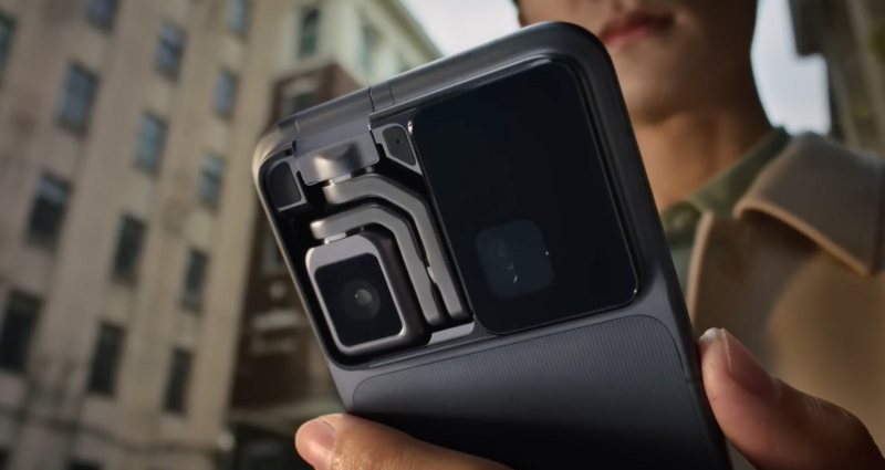 Close-up of a compact camera's back panel and articulating screen held up against an urban building backdrop.