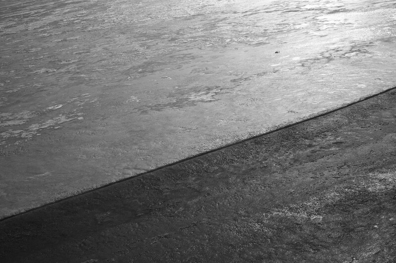 Black and white photograph of a diagonal line dividing wet and dry pavement surfaces.