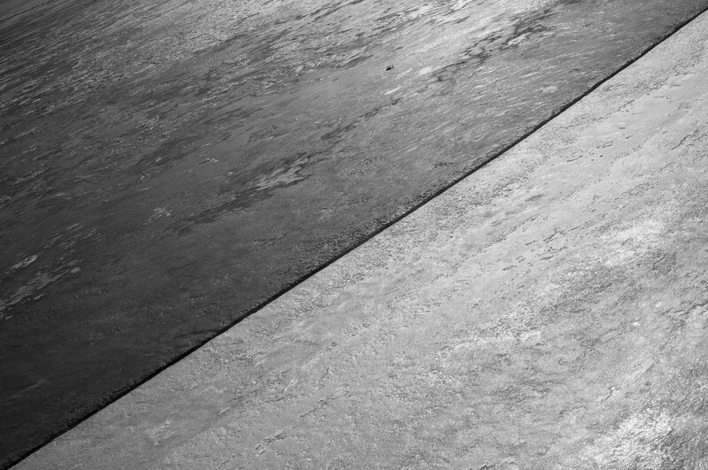 Diagonal seam dividing two concrete surfaces with contrasting tones and weathered textures.