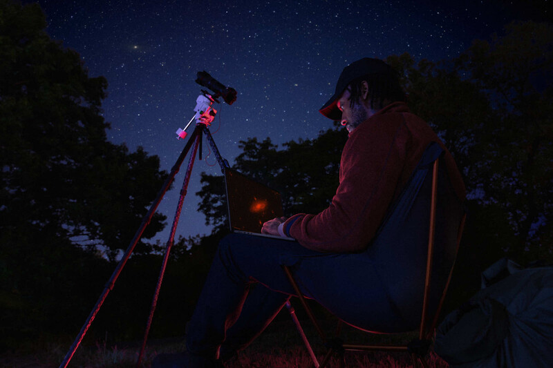 Astronomer observing the night sky through a telescope mounted on a tripod at dusk.