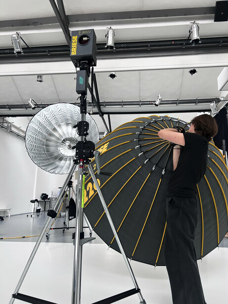Photographer adjusting a large octagonal softbox reflector on a C-stand in a studio setting.
