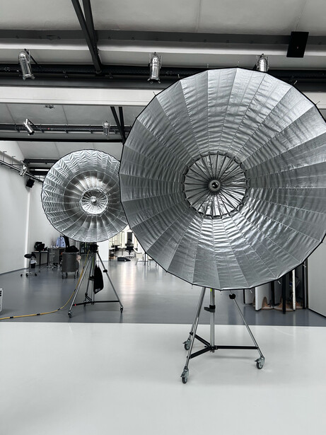 Two large reflective parabolic dish lights mounted on stands in a studio with industrial ceiling.
