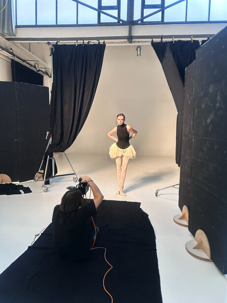 Fashion model posing during a studio photoshoot with professional lighting setup and black drapes.