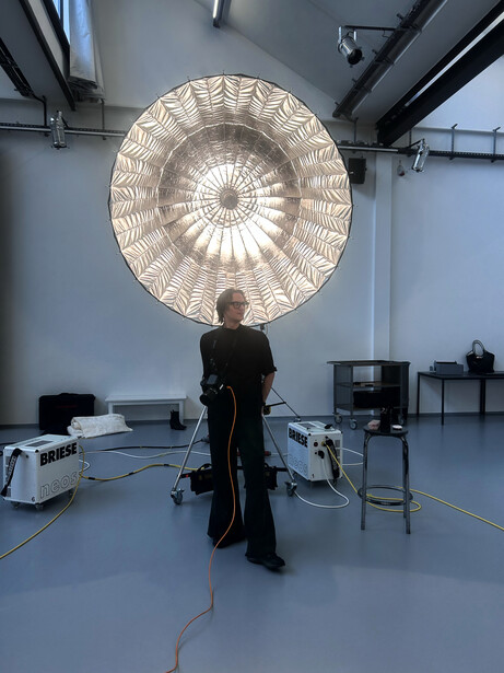Photographer standing beneath a large circular softbox suspended from studio ceiling rigging.