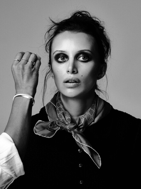 Black and white portrait of a woman with hand near face, wearing dark clothing and patterned scarf.