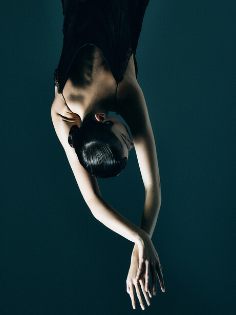 Overhead view of a pale-skinned arm holding a black boxing glove against a teal background.