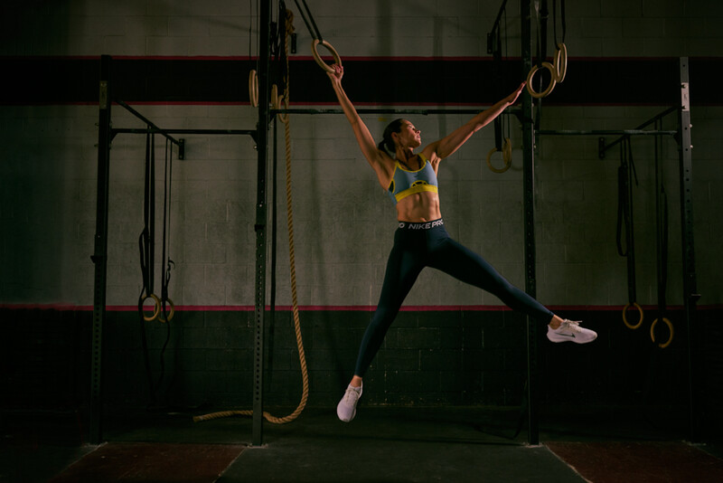 Athlete performing a gymnastics move on suspended rings with legs extended in a gym.