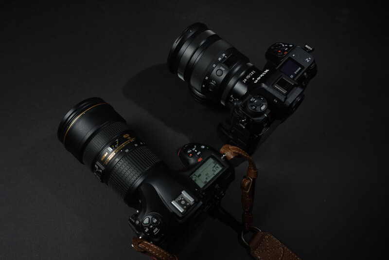 Two DSLR cameras with telephoto lenses arranged on a dark surface with a brown leather strap.