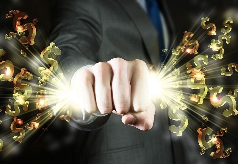 Businessman's clenched fist with golden dollar signs and light bursting outward against dark background.