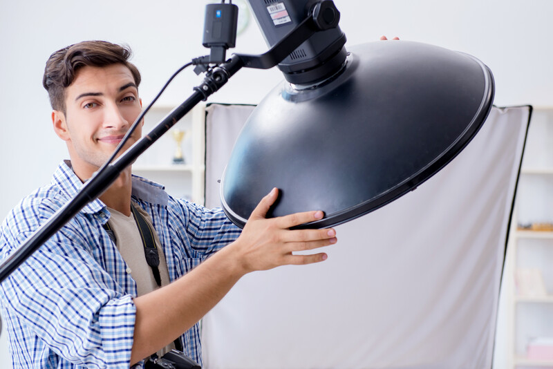 Photographer adjusting a large black studio reflector mounted on a boom arm above a white backdrop.