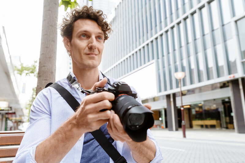 Photographer holding a DSLR camera with a strap in an urban plaza setting.