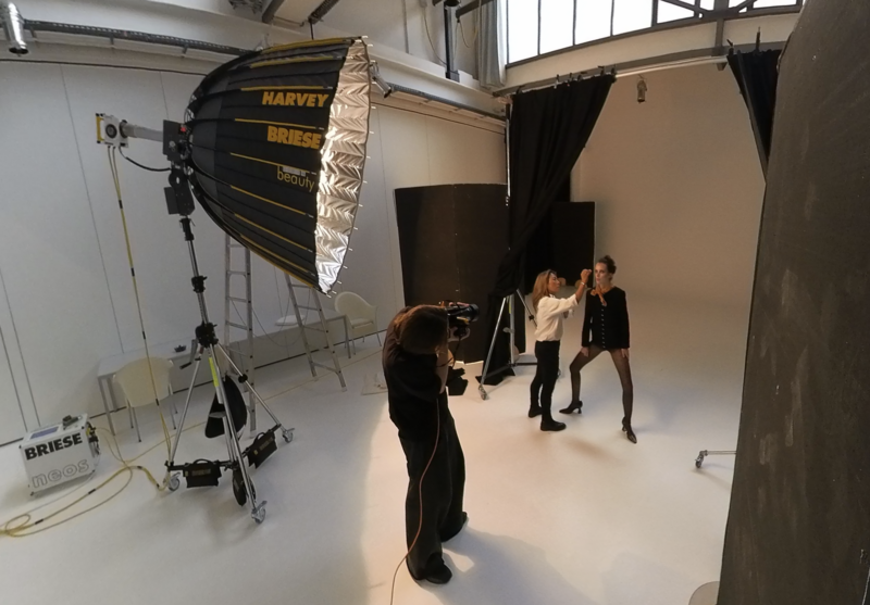 Professional studio setup with large parabolic softbox and crew positioning subject for a photoshoot.