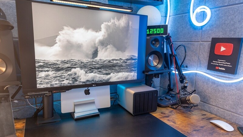 Content creator workspace with monitor displaying ocean wave photograph, professional lighting setup, and neon YouTube branding.