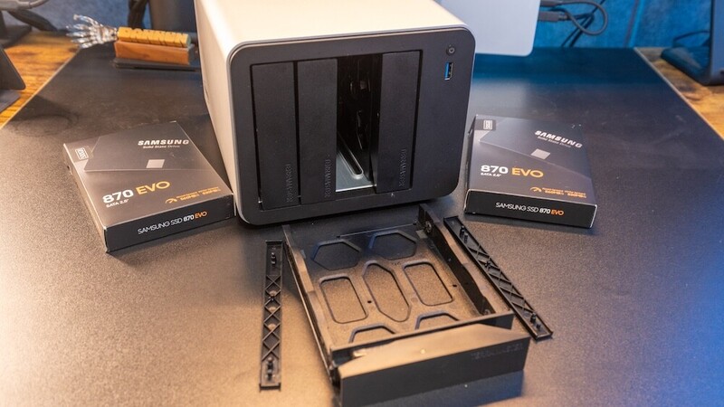 NAS storage enclosure with multiple Samsung 870 EVO SSDs and drive trays displayed on wooden desk.
