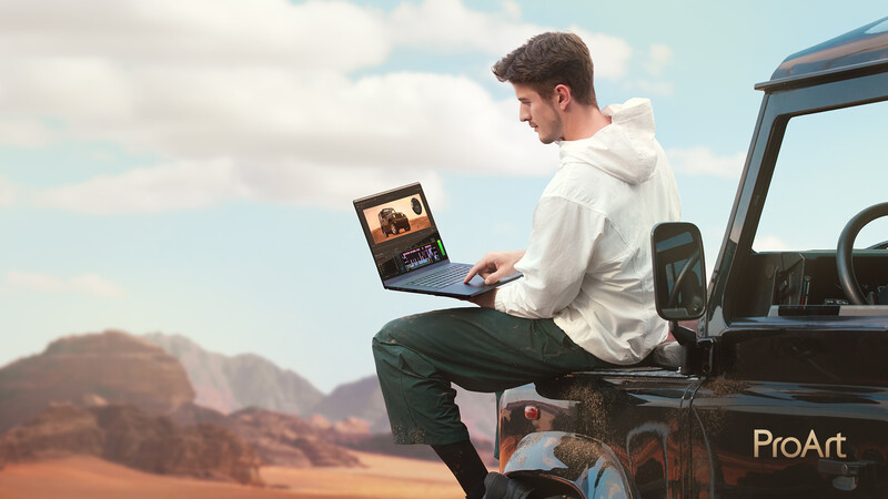 Man sitting on a vehicle tailgate working on a laptop with desert landscape in background.