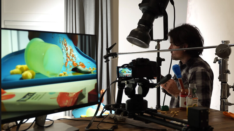 Filmmaker adjusting a studio light rig above a flat-lay food photography setup displayed on monitor.