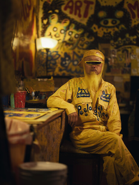 Person in yellow jacket seated in warmly-lit interior space with decorative wall panels behind.