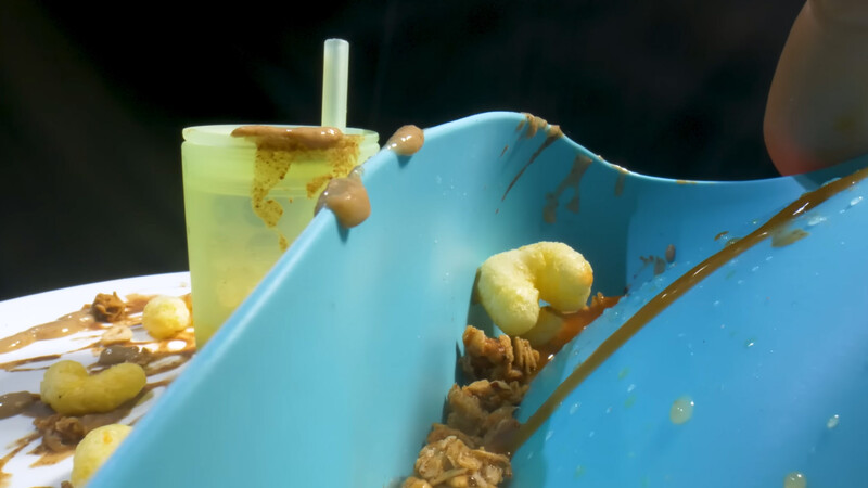Blue bowl containing food debris and a glass of pale yellow beverage with a straw in soft outdoor lighting.