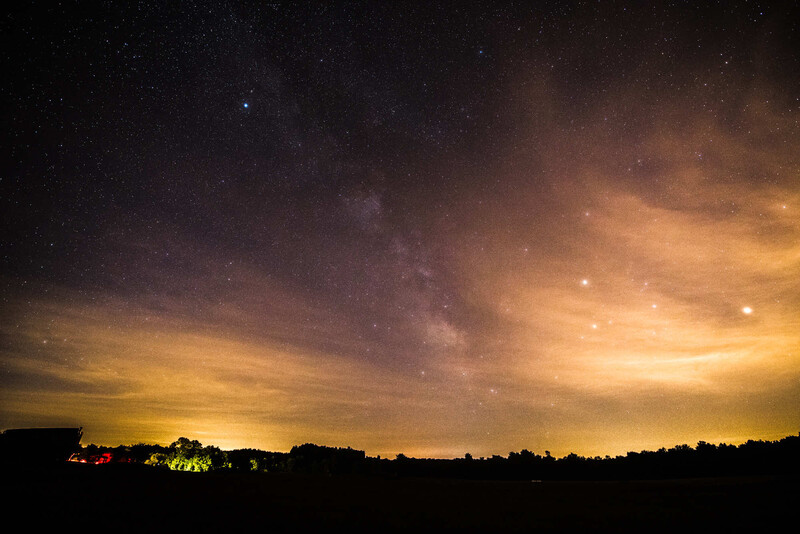 Milky Way visible above a darkened landscape with warm golden light on the horizon and stars scattered across the night sky.