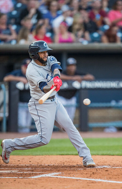 Baseball player mid-swing during a game, connecting with pitch as ball travels toward bat.